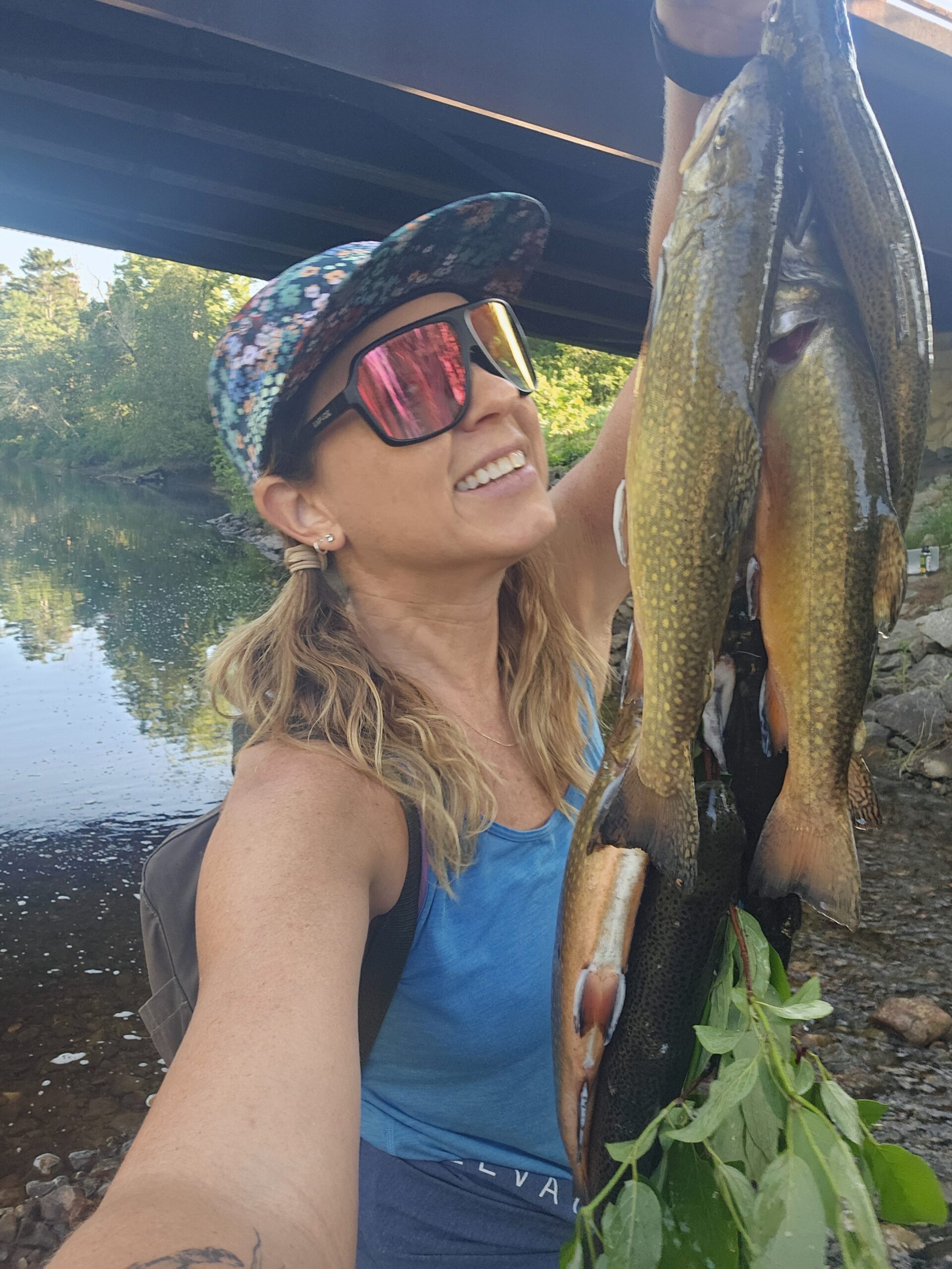 Stephanie holding up a stringer of brook trout by the river